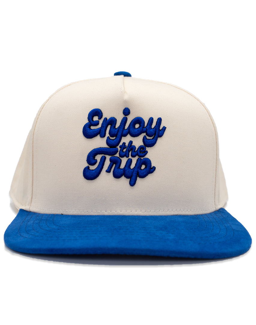 A two-tone Dodger Blue snapback cap with 'Enjoy the Trip' on the front, featuring a white crown and a blue visor.