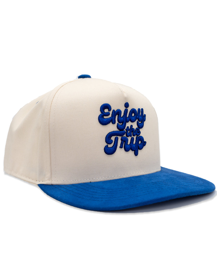 A two-tone Dodger Blue snapback cap with 'Enjoy the Trip' on the front, featuring a white crown and a blue visor.
